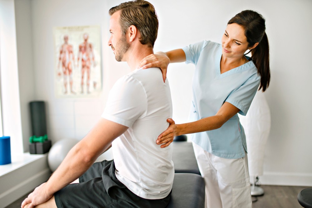 Physiotherapist touching back of male sitting upright on massage table