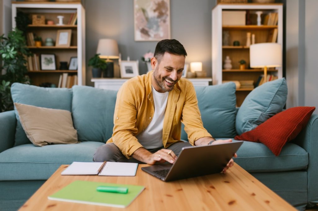 Male in living room smiling while using laptop