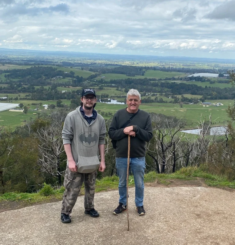 Two males standing on a hiking trail overlooking a scenic country backdrop